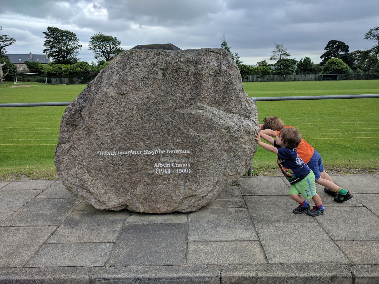 Two little boys pushing against the boulder